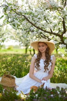 The beautiful girl the blonde in the blossoming apple-trees garden. White flowers in a garden in sunshine. Spring apple trees in blossom. Beautiful woman among spring blossom