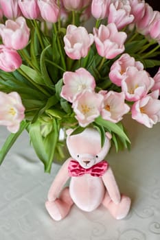 Pink bear toy and a vase with pink tulips on a table. Decor. Selective focus.