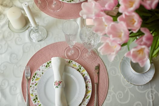Decor and spring table setting is a vase with pink tulips and dishes of white color. Selective focus.