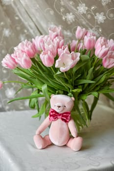 Pink bear toy and a vase with pink tulips on a table. Decor. Selective focus.