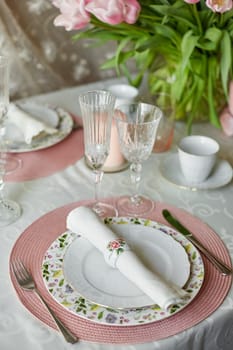 Decor and spring table setting is a vase with pink tulips and dishes of white color. Selective focus.
