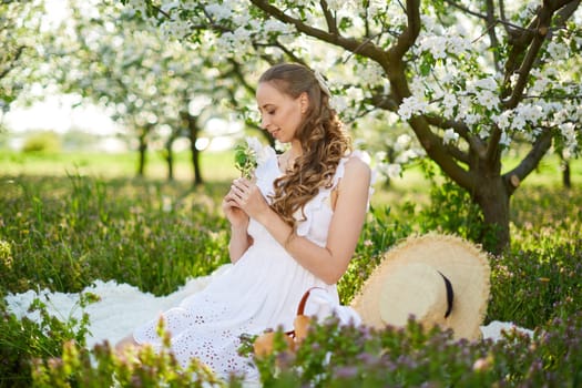 The beautiful girl the blonde in the blossoming apple-trees garden. White flowers in a garden in sunshine. Spring apple trees in blossom. Beautiful woman among spring blossom