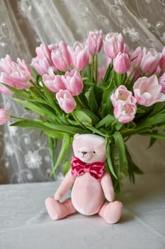 Pink bear toy and a vase with pink tulips on a table. Decor. Selective focus.