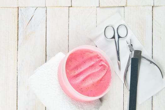 A set of cosmetic tools for manicure and pedicure on a blue background. Scrub, manicure scissors, white floor, nail clippers and a saw stand on a white wooden table top view with clear space.