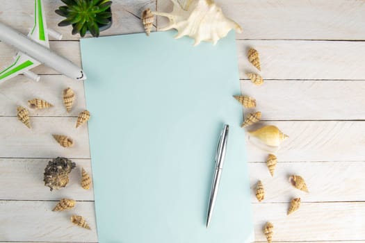 Sea shell, airplane and pen on a blue paper background on white wooden table. Vacation concept. Top views with clear space.