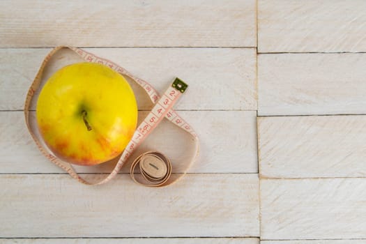 Healthy lifestyle concept. Yellow apple and centimeter on white wooden table close-up and copy space. Fruit Diet Concept.