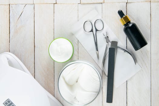 A set of cosmetic tools for manicure and pedicure on a blue background. Cuticle cutters, manicure scissors and hand oil stand on a white towel that stands on a white wooden table top view with clear space.