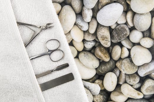 A set of cosmetic tools for manicure and pedicure. Manicure scissors, cuticles, saws on white towel stand on sea stones background. Top views with clear space.