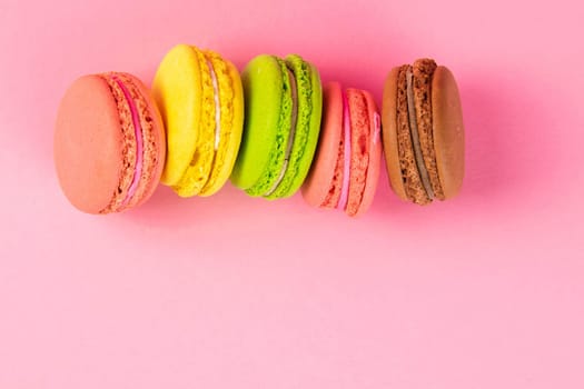 Colorful macaroons stand on a pink background. Top views with clear space