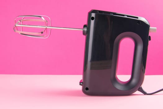 Kitchen electric hand mixer for mixing whip or eggs on pink table near a pink background. Close-up.