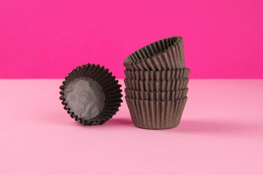 Pinc background with brown paper forms for muffins. Close-up.