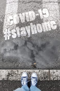Feet of a man in sneakers shoes standing on gray sidewalk with hashtag #stayhome (COVID-19). Coronavirus in the world. COVID-19 alert banner. 2019 Coronavirus concept, for an outbreak occurs in Wuhan - China.