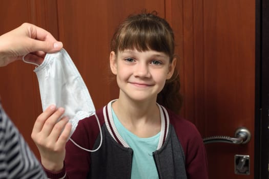 A girl takes a protective medical mask from her mother’s hand