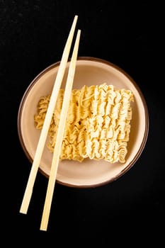 Instant noodles with wood sticks. Asian fast food on a black background close-up. Top views.