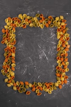 Pasta Conchiglie Rigate, mix of colorful uncooked shells in the shape of a rectangle with an empty middle. Textured Italian food background concept. Top view flat lay close up, clear space.