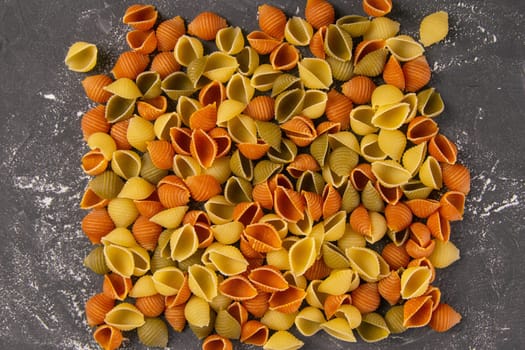 Pasta Conchiglie Rigate, mix of colorful uncooked shells In the shape of a square. Textured Italian food background concept. Top view flat lay close up.