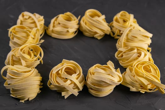 Raw tagliatelle pasta noodles frame and border isolated on black background, top view with clear space