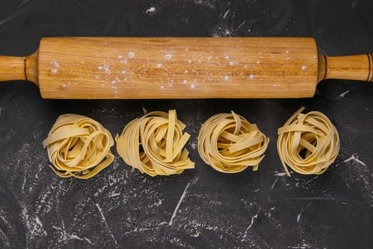 Raw tagliatelle with rolling pin for dough on black background. Top views with clear space