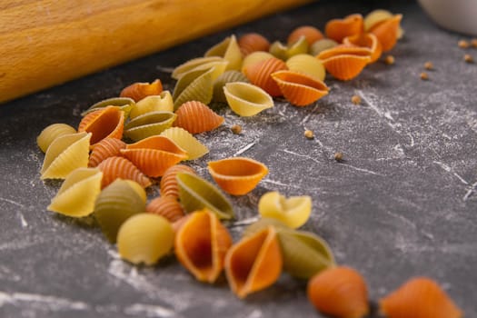 Pasta Conchiglie Rigate, mix of colorful uncooked shells with rocking for dough. Textured Italian food background concept. Top view flat lay close up, clear space.