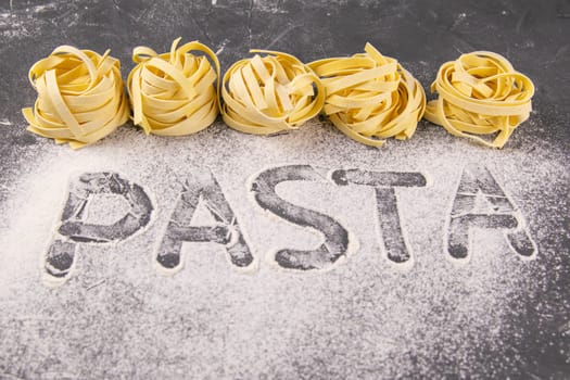 Homemade uncooked pasta tagliatelle on black background. Making fresh italian tagliatelle . The word 'pasta' from flour. Banner.