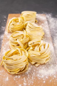 Variety of italian homemade raw uncooked pasta spaghetti and tagliatelle with flour on wooden board over black texture background. Front views.