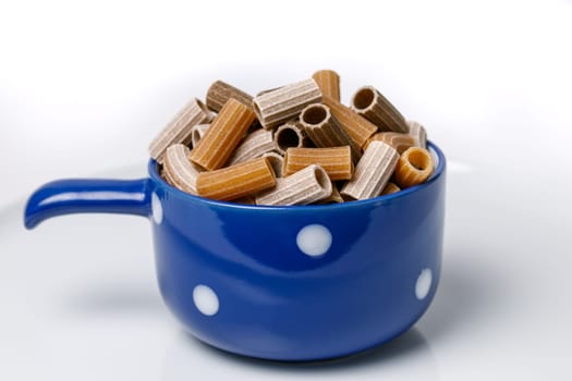 Three-colored pasta in a blue ceramic cup on a white background
