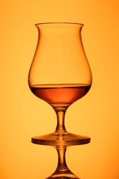Glass with orange whisky in back lit with reflection
