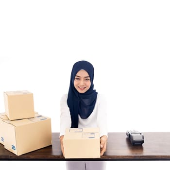 E-Commerce asian muslim women merchant work from home on wooden table with postal parcel cardboard boxes for shipping orders. Studio shot on white background for Selling online and small business SME.
