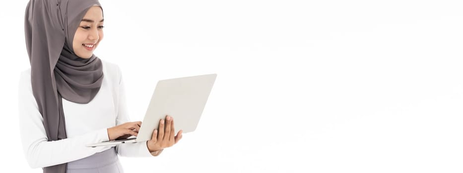 Asian young adult woman wearing hijab using laptop work from home to search and doing office work standing on white background - office, business, finance and work station concept