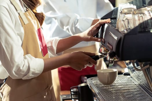 close-up shot of a barista brewing coffee by modern coffeemaker machine to making a cup of coffee with other barista working in background. Using for small business entrepreneur owner concept.