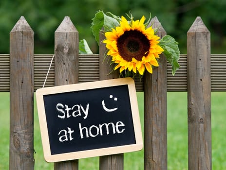Chalkboard with text and sunflower on garden fence, stay at home with smiley, corona virus protection