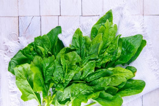 Freshly harvested spinach on a white towel, stand on white wooden table. Top views.