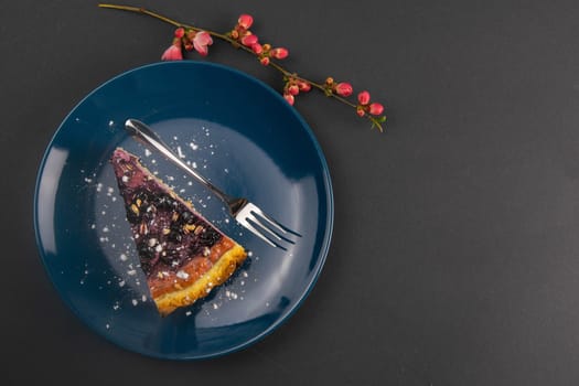 Slices of blueberry mousse cake with mirror glaze decorated berries and leaves of mint on a blue plate with red flowers are on black table, close up. Top views.