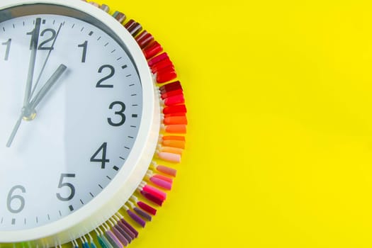 A set of cosmetic tools for manicure and pedicure on a blue background. The watch and palette of colors for manicureons on tips stands under the clock all standing on a yellow background.