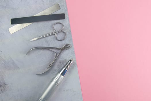 A set of cosmetic tools for manicure and pedicure. Manicure scissors, cuticles, saws, miller stand on a concrete pink background. Top views with clear space.