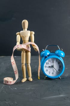Wood Figure Mannequin with measuring tape and blue clock, dieting Concept. Close-up