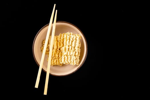 Instant noodles with wood sticks. Asian fast food on a black background close-up. Top views.