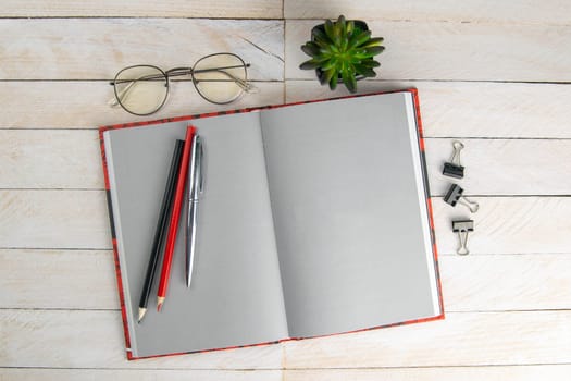 Open notebook, pen, glasses and green flower on a gray wooden background, texture. Office and holiday concept, place for the inscription. top view with clear space