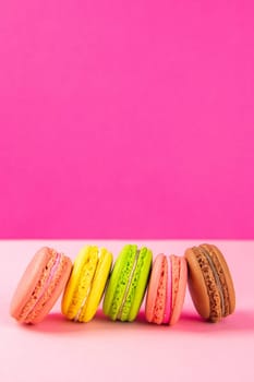 Colorful macaroons stand in a row against a pink background. Close-up with clear space