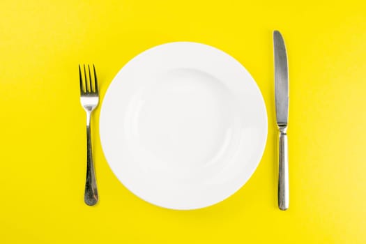Knife and fork on white plate. Creative food concept. Top views, close-up with clear space.