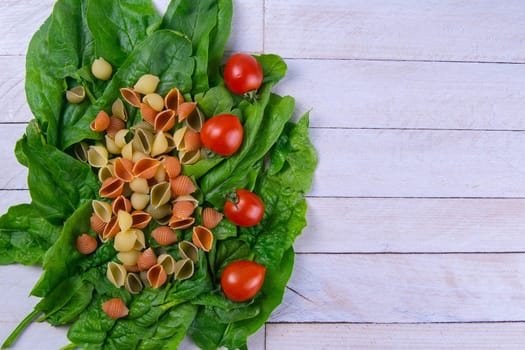 Raw conchiglie pasta with spinach and tomato. Italian Cuisine. Vegan food. Top views, close-up, clear space