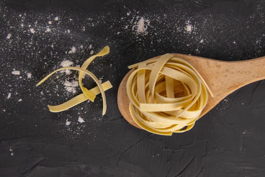 Raw pasta on a wooden spoon stand on a black background. Top views.