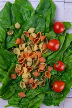 Raw conchiglie pasta with spinach and tomato. Italian Cuisine. Vegan food. Top views, close-up.