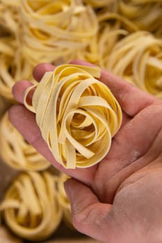 Homemade italian pasta. Woman's hand holds tagliatelle over the background of the pasta tagliatelle background. Top views.