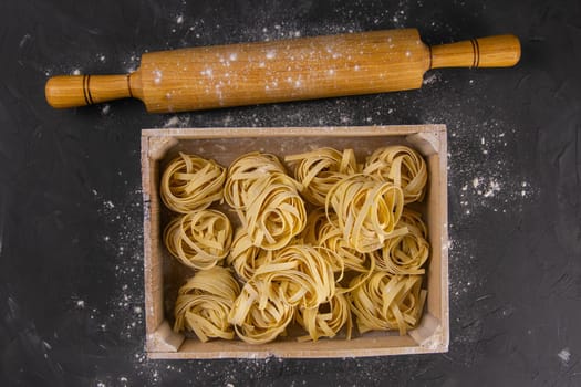 Still life of preparing pasta on rustic wooden background. Raw tagliatelle in a wooden box with rolling pin for dough and eggs. Top views.