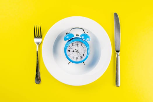 Alarm clock with fork and knife on the blue plate on blue table. Time to eat, Breakfast, Lunch Time and Dinner concept