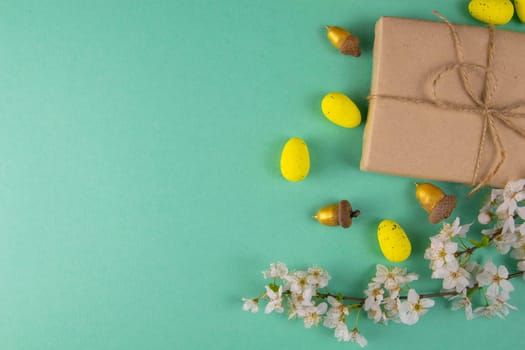 Two easter gifts, yellow eggs and white spring flowers on a mint background close-up. Easter background.