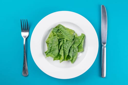 Fresh green spinach leaves on a white plate fork knife on bright yellow background flat lay top view copy space. Baby young spinach leaves, healthy food, diet. Creative food concept.