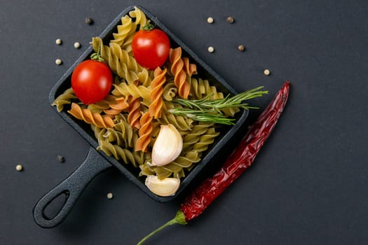 Italian food raw pasta fusilli with tomatoes, rosemary, hot pepper and garlic in a small frying pan. Top views, close-up