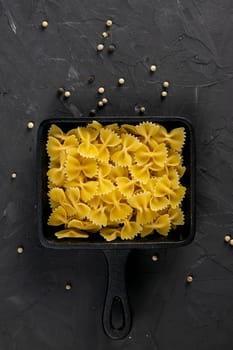 Raw pasta farfalle in frying pan on dark background. Top views, close-up.